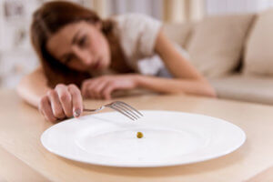 A woman exhibits physical signs of an eating disorder by struggling to eat a single pea
